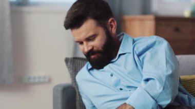 Sıradan bir erkek şık, modern bir oturma odasındaki rahat bir kanepede dinlenirken rahat bir şekilde akıllı telefon kullanır.