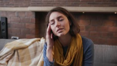 Kanepede oturan baş ağrısı çeken genç bir kadının yüzünü kapayın. Hasta hissedin. Mutsuz, mutsuz, kadın semptomları.