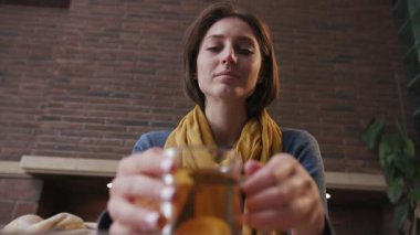 Aşağıdan bir çerçeve. Genç kadın çay içiyor. Etrafına bak. Kanepe ateşine oturmuş gülümse.