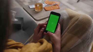 Kapalı el telefonu kullanan yeşil ekranlı kadın yaşam odasının arka planında kanepede otururken birçok farklı dönen uyuşturucu teknolojisi krom anahtarı ağır çekimde