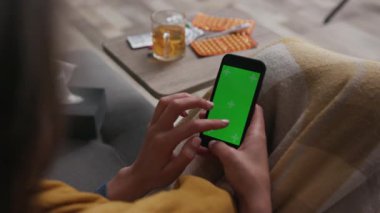 el telefonu kullanan, dikey yeşil ekranlı bir kadın yaşam odasındaki kanepede otururken arka plan çayı birçok farklı dönen uyuşturucu teknolojisi krom anahtarı yakın çekim