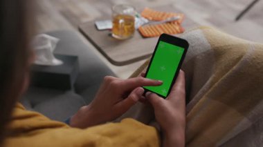 Ağır çekimde çalışan kadın yeşil ekranlı akıllı telefonu kullanarak yaşam odasındaki kanepede otururken arka planda birçok farklı dönen uyuşturucu teknolojisi kromu kullanıyor.