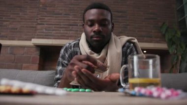 Afro-Amerikan portresi. Kanepede oturan genç adam, telefona bak. Kameraya bak, evde hap iç.