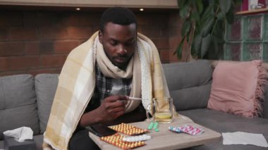 Mutsuz Afro-Amerikalı genç adam kanepe ateşinde oturuyor. Evde telefon kullanıyor. Çay içiyor. Mutsuz, grip, hasta, soğuk algınlığı hastası.