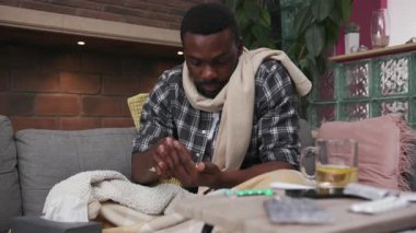 Afrikalı Amerikalı genç adam kanepede uzanıyor. Evde çay içiyor. Üzgün, mutsuz, grip, hasta, soğuk algınlığı, virüs alerjisi.