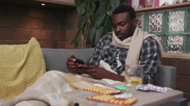 Afro-Amerikan portresi. Kanepede uzanmış. Evde telefon kullanıyor. Çay içiyor.