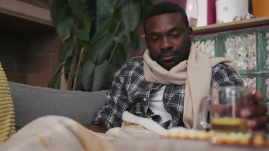 Yakışıklı Afro-Amerikalı genç adam kanepede oturuyor. Evde çay içiyor. Mutsuz, grip, hasta, soğuk algınlığı hastası, virüs alerjisi.