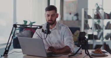 Kameraya gülümseyen dizüstü bilgisayar ve mikrofon kayıt podcastı kullanan profesyonel video blogger beyaz tenli yetişkin portresi.