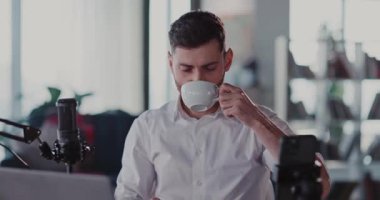 Başarılı yetişkin beyaz adam podcast video blogunu bitiriyor kahve içiyor ve koltukta dinleniyor..