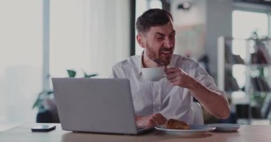 Komik sakallı adam sıcak bir dairede kalıyor, kruvasan yiyor ve kahve içiyor, evde internetten komik videolar seyrediyor..