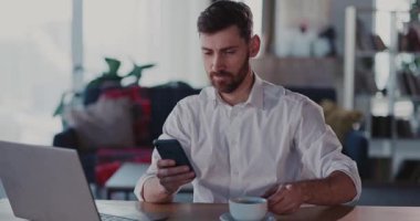 Bir adam, şık ve modern bir çalışma alanıyla çevrili bir akıllı telefonu kullanırken aktif olarak işle meşgul.
