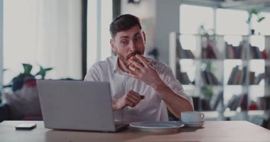 Beyaz tenli heyecanlı milenyum hayranı dizüstü bilgisayardan eğlenceli videoiçerikler izliyor sosyal medyada, ayçöreği yiyor ve sabahları kahve içiyor..