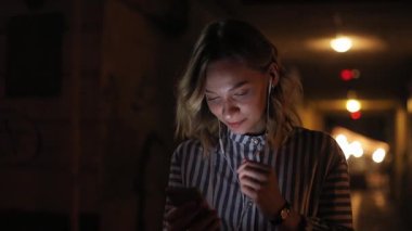 Portre çekici genç bir kadın telefon kullanıyor. Kulaklıkla müzik dinliyor. Kasabanın sokaklarında yürürken.