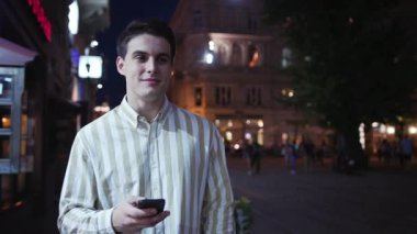 . Çekici genç adam akıllı telefon tebessümü kullan. Etrafına bir bak. Gece turist, modern iş adamları.