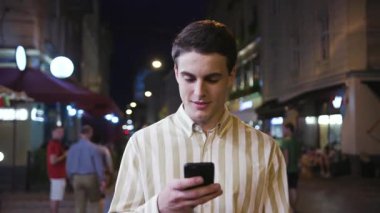 Çekici genç adam, akıllı telefon tebessümü kullan. Geceleri turist, modern, yakışıklı iş adamları. Elinde cep telefonu, elinde yaşam tarzı cep telefonu.