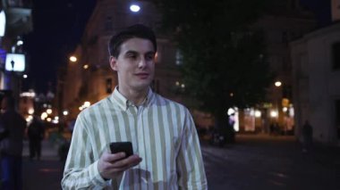 . Çekici genç adam akıllı telefon tebessümü kullan. Etrafına bir bak. Gece turist, modern iş adamları.