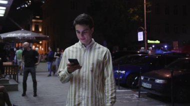 Çekici genç adam, akıllı telefon tebessümü kullan. Gece kameraya bak. Turist, modern iş adamları.