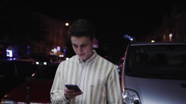 Kameraya bak, çekici genç adam geceleri akıllı telefon standı kullanıyor. Turist, modern iş adamları. Elinde cep telefonu, elinde yaşam tarzı cep telefonu var.