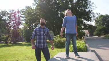 Uçurtma uçuran sıradan giysili beyaz bir adam. Yakışıklı baba oğlunun yanında duruyor, çak bir beşlik. Açık havada. Yaz zamanı. Arkaplanda yeşil park