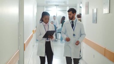 Çok ırklı çift, beyaz sakallı terapisti olan Afro-Amerikan doktor koridorda yürüyor ve konuşuyor. İş arkadaşları. İşbirliği. Tıbbi personel. Hastane.