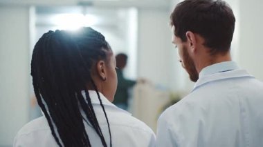 Koridorda yürüyen ve hasta raporlarını evde tartışan baş doktor ve bayan Afro-Amerikalı kadın asistanların yakın çekimleri. Hastane ortamı. Sağlık çalışanları..