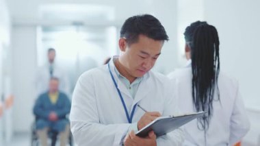 Hastanenin koridorunda gülümseyen kameralar için klinik kayıtlar yazan Çinli doktor portresi. Sağlık hizmetleri. Sağlık personeli.