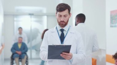 Kameraya gülümseyen yakışıklı beyaz erkek doktor terapist hastalara klinik kayıtlar yazmakla meşgulken. Profesyonel erkek portresi. Mesleğiniz? Tıbbi konsept.