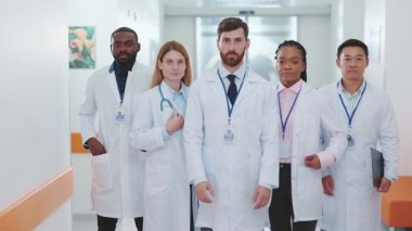 Laboratuvar önlüklü çeşitli tıp uzmanları yoğun bir hastane koridorunda güven içinde poz veriyorlar.