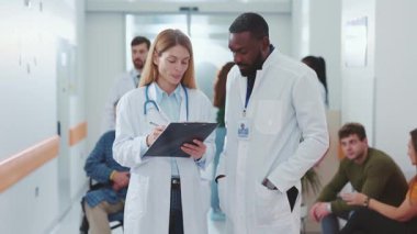 Sağlık uzmanları yoğun bir hastane koridorunda hasta bilgileriyle ilgili hayati tartışmalara giriyorlar.