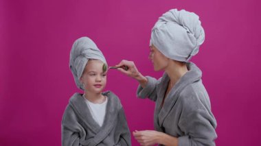 Beyaz tenli güzel ve mutlu bir anne ve kızı birlikte cilt bakımı yapıyorlar. Neşeli anne, bebek çocuklarına yeşim taşıyla masaj yapıyor. Kadınsı. Sağlık Hizmetleri.