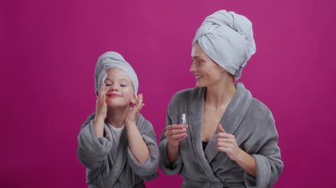 Güzel beyaz anne ve küçük kızı bornoz giyip aynanın önüne yüz serumu sürüyorlar. Aile bireysel bakımı. Cilt rutini. Kozmetik reklamları.