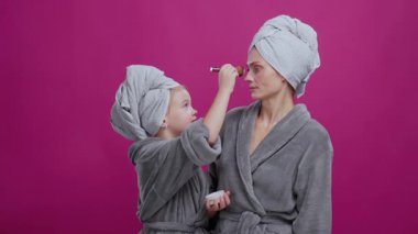 Anne ve kızı birlikte cilt bakımı ve makyaj yapıyorlar. Çekici anne kızının kozmetik tozu kullanmasına şaşırır. Eğlence ve güzellik konsepti.