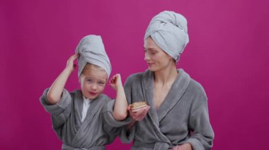Genç, beyaz bir anne ve kızı bornoz giyerek ve kafa havlusu giyerek birlikte makyaj yapmaya hazırlanıyorlar. Kozmwtik reklamlar.