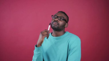 Gözlüklü, keçeli kalemle düşünen, iyi bir fikir bulan zeki bir genç. Güzel renkli duvarın arka planında kameraya bakan tatlı, ciddi bir Afrikalı öğrenci..