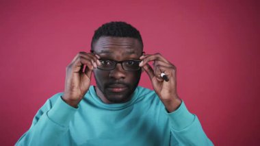 Gözlük takan yakışıklı bir gencin portresi. Sıradan kıyafetler giyen akıllı, düşünceli Afrikalı adam doğrudan kameraya bakıyor. Yakın plan. Güzel renkli duvar.