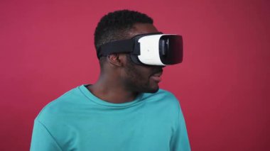 Sanal gerçeklik gözlüklü sevimli bir adam, etrafa bakıyor, pembe duvarın arkasında kavga ediyor. Genç ve çekici Afrikalı bir adam kameraya bakıyor. Parlak beyaz bir gülümseme. Yakın plan..