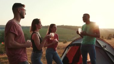 Bir grup arkadaş, gün batımının muhteşem manzarasının tadını çıkarırken rahat çadırlarının dışında içkileriyle sevinçle kutluyor.