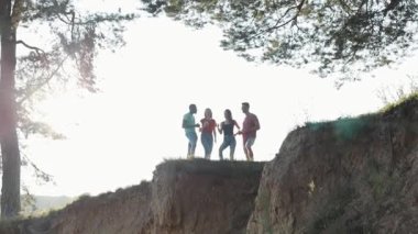 Yüksek bir tepede dikilen genç insanların uzak hava manzarası. Parlak güneş ışığında içkileriyle iletişim kuruyor ve neşeleniyorlar. Aktif yaşam tarzı, turizm konsepti, özgür hissetmek. Birlikte mutluyuz