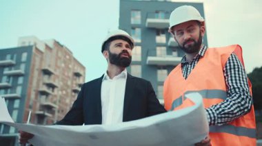 Müteahhit ve işadamı modern iş merkezinin inşaat planını tartışıyorlar. Klasik kostümlü bir adam uzaktan başını sallıyor. Düşük açılı çekim, yakın görüntü