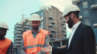 Çok ırklı profesyonel inşaat işçileri, lüks takım elbiseli, genç ve ciddi bir iş adamıyla bir projeyi tartışıyorlar. Para kazanmak, işbirliği.