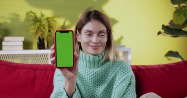 Model akıllı telefon yeşil ekranlı, kameraya gülümseyen, modern uygulama alışverişini kullanarak evde kalan güzel bir kadın. Sıradan insanlar..