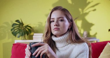 Gündelik kıyafetli, evde dinlenen kahve içen çekici genç bir kadın. Hoş, samimi, kızıl bir kızın portresi sıcak içeceklerle evde dinleniyor..