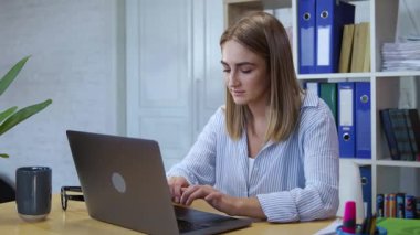 Modern şirket ofisinde klavye dizüstü bilgisayarında yazı yazan hırslı genç bir kadın. Halk ve meslek.