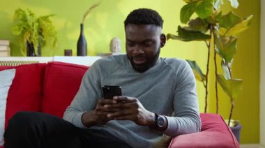 Afro-Amerikalı genç adam sosyal ağlara göz atıyor. Haberleri okuyor, sürpriz bir şekilde mesaj yazıyor. Evde iyi vakit geçiriyor..