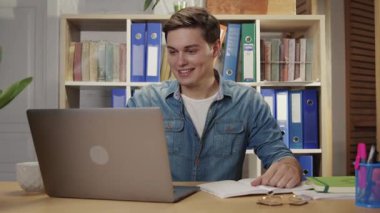 Ofis müdürü olarak çalışan çekici ve zeki genç bir adam müşterilerle çevrimiçi iletişim kuruyor modern netbook bilgisayarını kullanarak ofis ortamında notlar alıyor. İş adamı.