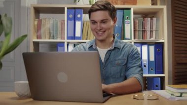 Laptop bilgisayarında gülümseyen, iş yerinde arkadaşlarıyla sohbet eden, ofiste boş vakitlerin keyfini çıkaran olumlu genç adam..