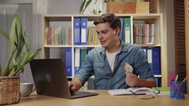 Genç adam ofiste çalışıp laptoptan para kazanıyor. Başarılı çalışan internet üzerinden hızlı zengin oluyor..