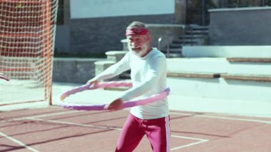 Neşeli bir son sınıf öğrencisi, güneşli bir spor sahasında renkli hula hoop 'u kullanarak eğlenceli ve ilgi çekici bir oyundan zevk alır.