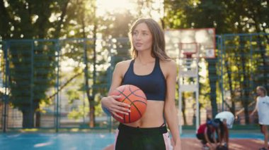 Kendine güvenen genç bir kadın canlı bir basketbol sahasında elinde basketbol topuyla poz veriyor.