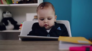 Şık bir takım elbise giymiş inanılmaz derecede sevimli küçük bir bebek masasında renkli bir tableti keşfediyor.